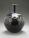 Photo couleur montrant une bouteille en terre cuite sur fond gris.