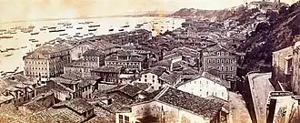 Vue plongeante du sommet d'une colline donnant sur les immeubles d'une ville avec un port encombré de divers navires en arrière-plan
