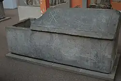 sarcophage en pierre couvercle à demi-soulevé. Divers motifs gravés : deux lions, un paon, un symbole christique, une fontaine