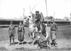 Photographie en noir et blanc représentant un cavalier entouré de quatre personnes, dont une assise par terre.