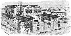 Gravure représentant une usine, avec de grands corps de bâtiments en brique sur plusieurs étages et une cheminée.