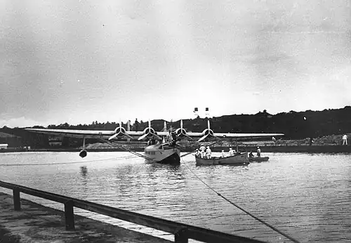 photo N&B. Hydravion quadrimoteur dans un chenal, une barque à proximité