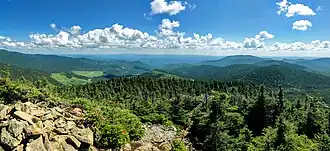 Vue d'un sommet rocheux sur des collines boisées.