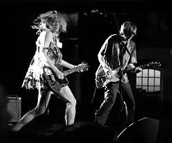 Une femme à gauche et une homm à droite sur scène tenant leur guitare respective.