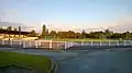 Terrain de football en herbe avec une tribune sur la gauche et une aire de lancer pour l'athlétisme en fond.