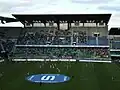 Photographie montrant une vue d'ensemble de la tribune Rennes et de ses spectateurs, avec un écran géant dans sa partie haute et la partie réservée aux supporters adverses sur son côté droit.