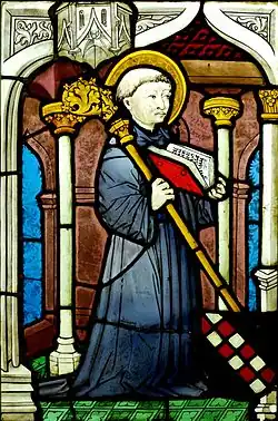 Vitrail d'un moine en robe noire, de trois-quart vers la droite et auréolé, tenant une crosse épiscopale et un livre ouvert, dans une église.