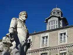 Vue en contre-plongée des étages supérieurs et du clocheton d'un bâtiment ; statue d'Henri IV au premier plan.