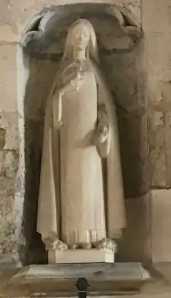 Statue blanche de femme tenant un crucifix avec, à ses pieds, un bouquet de roses.