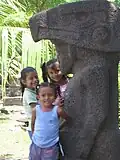 Des enfants se tiennent devant une idole de pierre précolombienne.