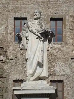 Statue d'un homme debout portant un livre ouvert dans sa main gauche.
