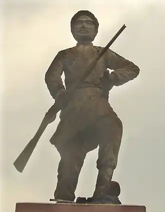Statue montrant un homme moustachu debout tenant un fusil et portant des vêtements traditionnels.