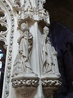 Photo montrant deux statues de saints évêques en pierre blanche sur les montants d'un tombeau monumental.