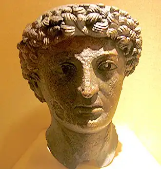 Tête en bronze vert, avec les cheveux bouclés formant une grosse couronne, à demi plongée dans l'ombre.