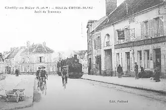 La route de Paris avec la façade de l'auberge à droite, photographiée pour une carte postale au tournant du XXe&nbsp;siècle.