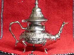 Théière décorée argentée sur fond de rideau rouge.