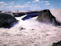 Vue de la brèche dans le barrage Teton le 5 juin 1976 : la retenue (en arrière-plan) se vide entre la paroi rocheuse (à gauche) et ce qui reste du barrage (à droite).