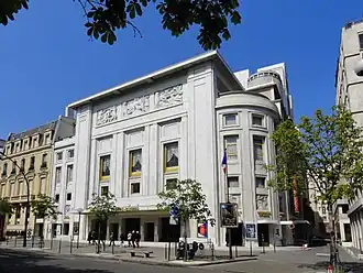 Grand bâtiment blanc cassé de style mixte art déco et classique d'environ 4 étages avec une grande entrée et des bas reliefs gravés au dernier étage