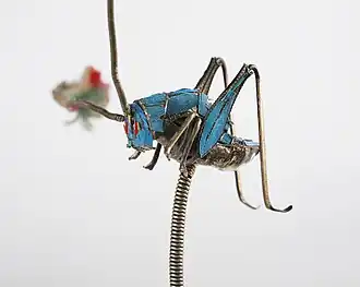 Une épingle à cheveux chinoise en forme de criquet avec des plumes de martin-pêcheur dans la collection permanente du Children's Museum of Indianapolis.