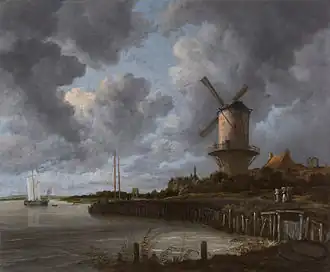 Grand moulin à vent au bord d'une rivière sous un ciel très nuageux.