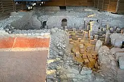 Vue de la salle chaude avec les pilettes du sol suspendu et au premier plan un mur avec un enduit rouge sur le mur extérieur.