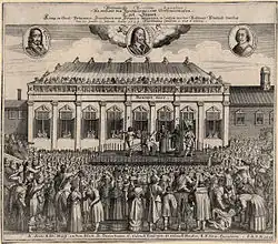 Vue d'une large foule rassemblée autour d'une estrade situé devant un bâtiment à colonnades. Sur l'échafaud, un homme vient d'être décapité et le bourreau montre sa tête à la foule.