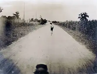 Un homme seul court au milieu d'une piste de terre, photographié depuis une voiture.
