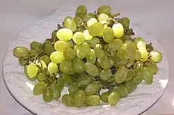 Photographie montrant une grosse grappe de sultanine ; les grains ovales sont vert-jaune. Leur pruine a partiellement été enlevée par le lavage.