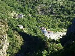 Photo couleur montrant une vallée montagneuse couverte de forêt. Dans la vallée, un bâtiment moderne haut de plusieurs étages.