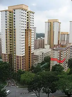 La photographie montre des immeubles d'habitation. Deux d'entre eux, au centre et à gauche, font 26 étages ; les autres sont plus petits. Un des appartements d'un immeuble sur la droite est coloré en rouge sur l'image pour être mis en avant.
