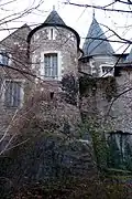 Photographie d’une tour d'habitation, d'aspect médiéval, en moellons, construite sur la roche, et coiffée d’un toit conique en ardoise.