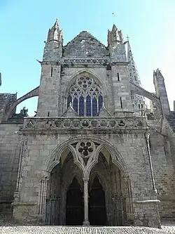 Une photo de façade d'église à deux niveaux, avec un grand porche central et au-dessus une grande baie à lancettes.
