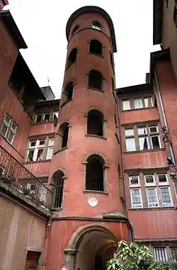 Photographie couleur d'un immeuble Renaissance, à la façade crépie en rouge, comportant au premier plan une tour à l'intérieur de laquelle s'élève un escalier d'accès en colimaçon.