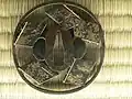Tsuba avec divers motifs et quelques Kanji, sur le haut de la pièce