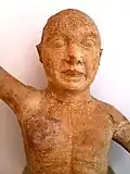 Photographie en couleurs représentant une statuette à la tête chauve et au torse nu.
