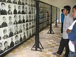Photographie couleur d'un homme regardant des portraits d'enfants fixés sur un mur.