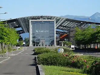 Photo sur l'entrée d'un bâtiment comprenant une grande porte vitrée et des toitures en acier.