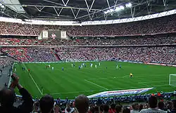 Vue à mi-hauteur depuis les tribunes d'un stade avec ses tribunes remplies avec un match en cours.