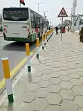 Arrêt de bus à Bouaké, trottoir à dalles hexagonales avec alignement de plots séparateurs au couleurs ivoiriennes, janvier 2024
