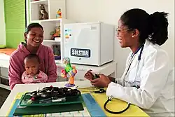 Une femme médecin en blouse blanche reçoit une mère et son enfant.