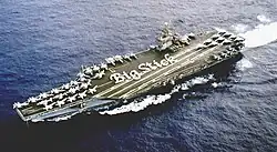 Vue aérienne du porte-avions ; les marins sont disposés de manière à écrire “Big Stick” sur le pont d'envol.