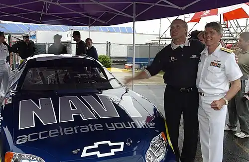 Deux hommes se tenant debout à côté d'une voiture de course bleue.