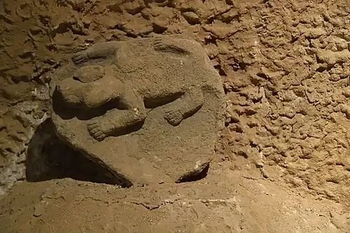 Pierre sculptée beige posée sur un tas de terre posée sur un mur de terre.
