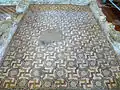 Mosaïque où on peut observer la tâche laissée par un feu au moment de l'abandon de la villa.