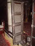 Gros plan sur un vantail de la porte. Il présente quatre panneaux carrés ajourés.