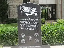 Une plaque de marbre noir gravé du drapeau américain en noir et blanc, suivi d'un texte honorant les militaires américains ayant donné leur vie.