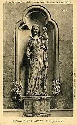 Dans une niche, statue en pierre, peinte, d'une femme tenant un enfant avec son bras gauche et une fleur avec son bras droit. L'enfant présente la tête d'un adulte.