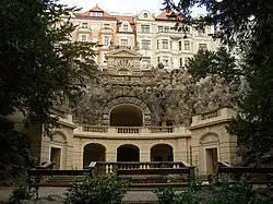 Čelní pohled na umělou jeskyni (grottu), před ní je kašna s fontánou.