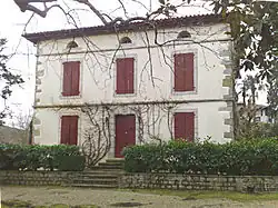 Photographie d’une maison à un étage, aux volets rouge sang clos.