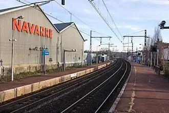 Vue de hangars industriels en bordure d'une voie ferrée ; enseigne « Navarre » et panneau SCNF « Villabé ».